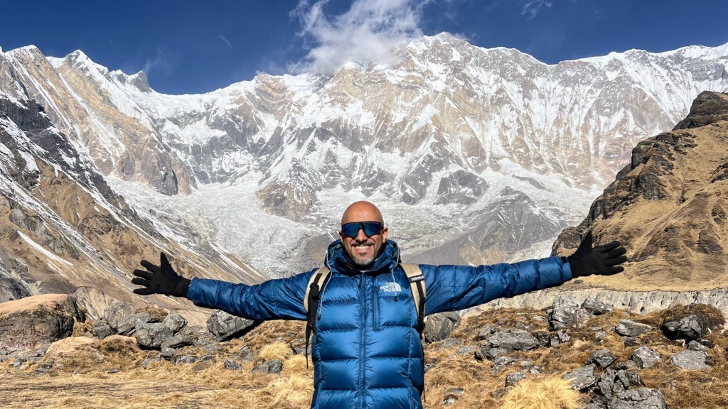 Mohamed Isa with arms outstretched below the snow-covered face of Annapurna, Nepal