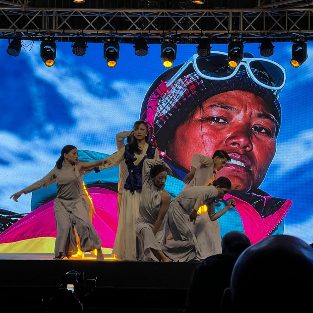 Dancers performing in front of a screen showing Pasang Lhamu Sherpa at the opening of the Ascent Summit