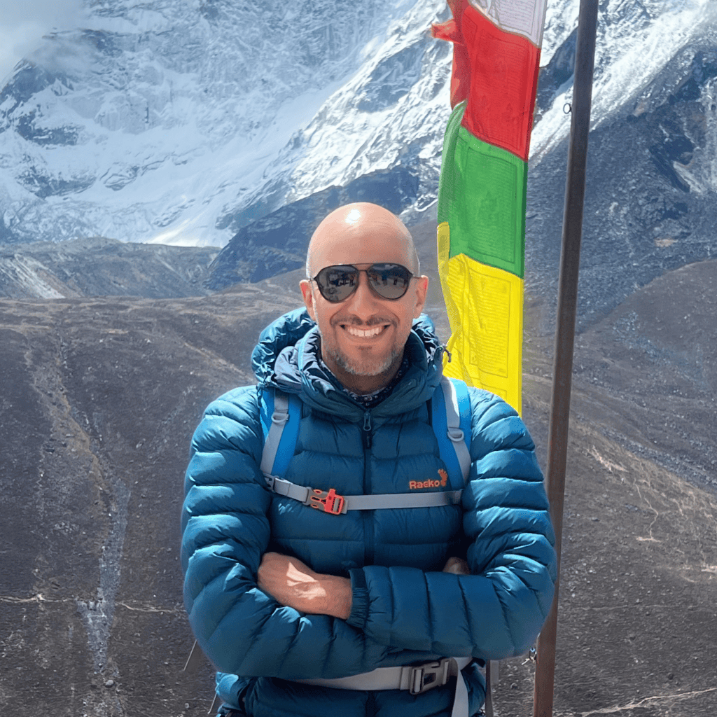 Mohamed Isa on the trail to Everest Base Camp, with prayer flags and a glacier behind him