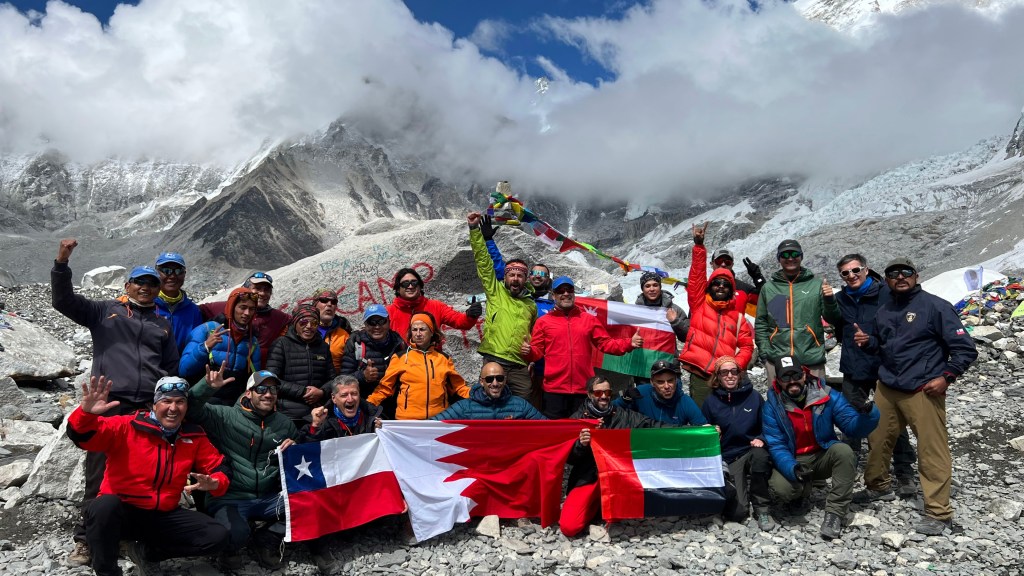 Mohamed Isa with fellow trekkers at Everest Base Camp, holding the Bahrain flag, with prayer flags and the Khumbu Icefall behind