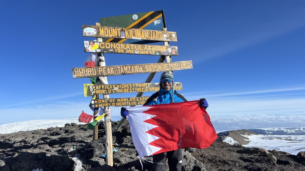 Mohamed Isa holding the Bahrain flag at the Uhuru Peak summit sign on Kilimanjaro, 5,895 meters