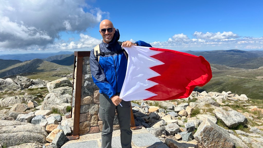 Mohamed Isa holding the Bahrain flag at the summit marker of Mount Kosciuszko, Australia