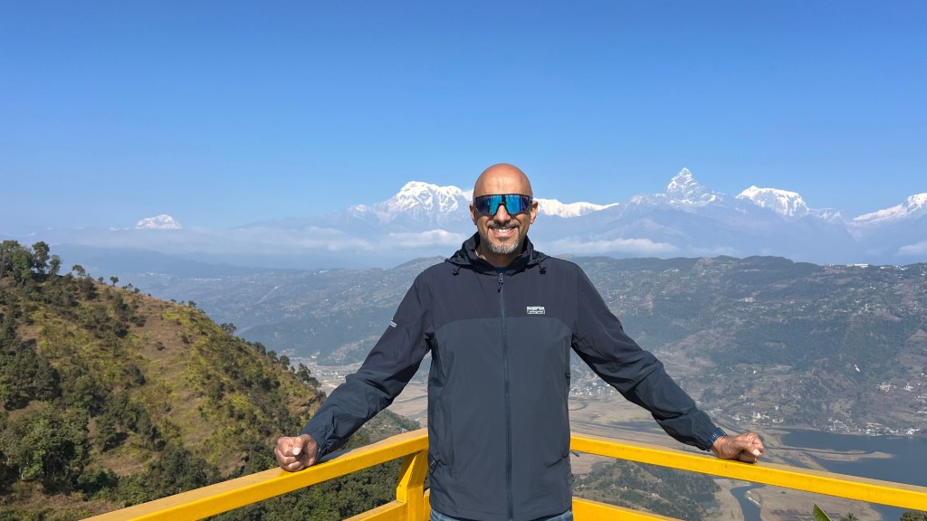 Mohamed Isa at a yellow railing above a lake and green hills, with the snow-covered Annapurna Range behind